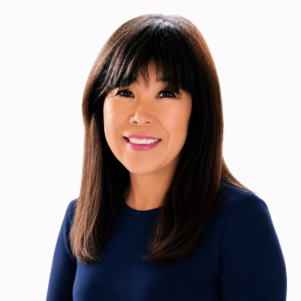 A woman with straight dark hair and bangs, wearing a navy blue top, smiles in front of a plain white background.